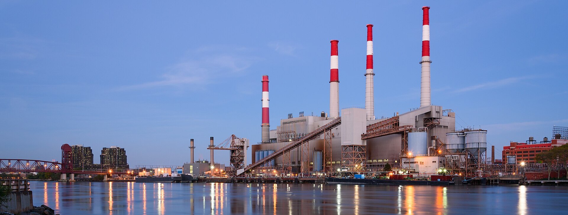 Ravenswood Generating Station at dusk on the East River in New York City, its four stacks lit against a blue evening sky